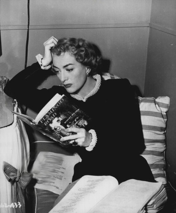 1949. On the set of 'Flamingo Road,' reading the novel by Robert Wilder.